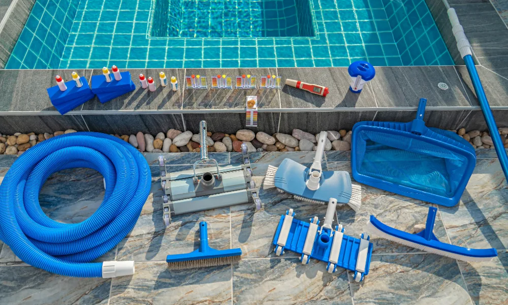 Pool cleaning equipment including vacuum hose, brushes and leaf net laid out beside a pool
